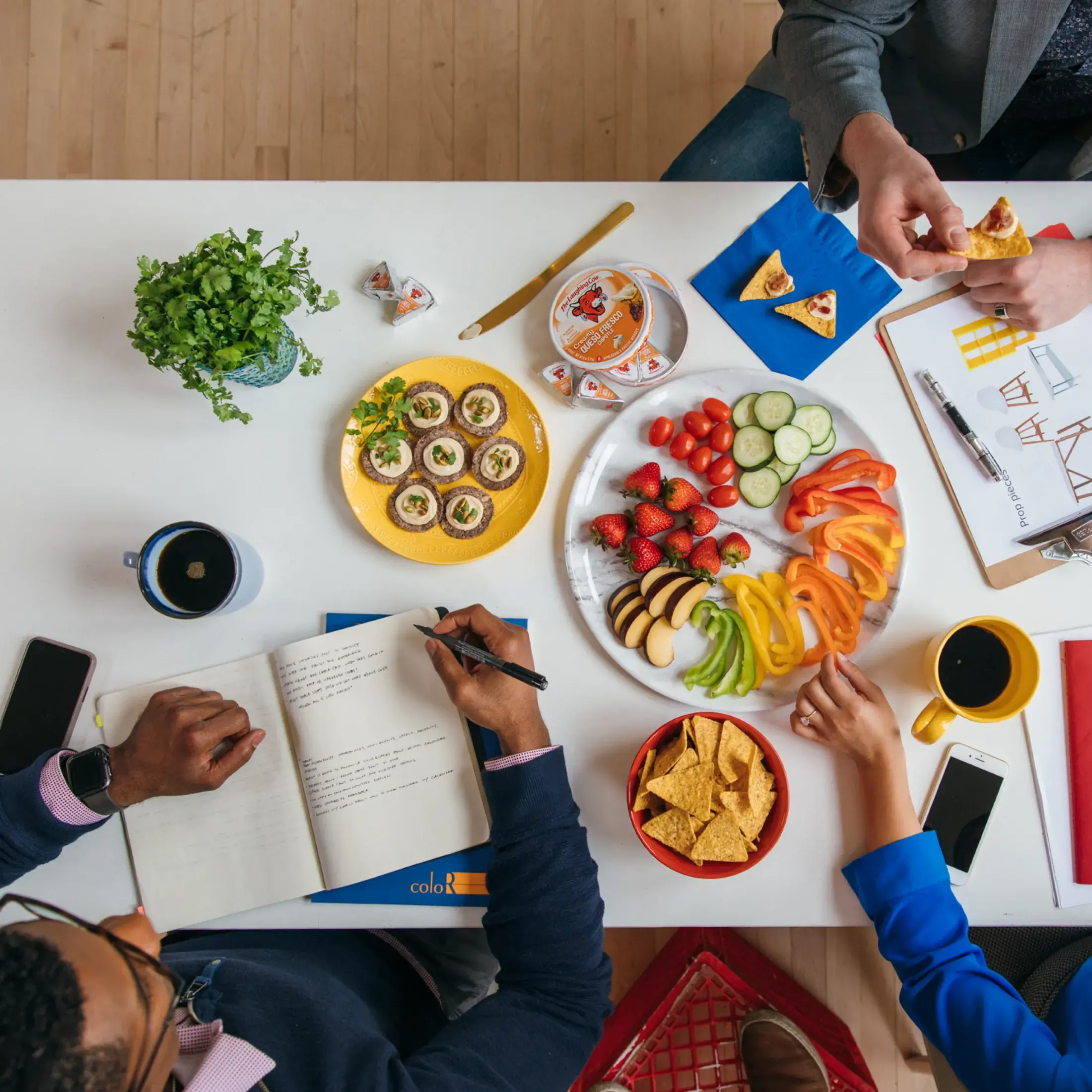 a group of three people doing work while enjoying snacks with Laughing Cow cheese