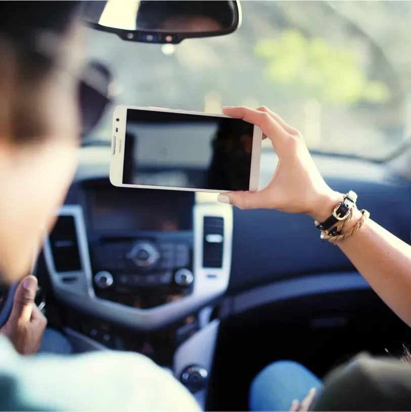 Over the shoulder shot of a man in a car looking at a Huawei Ascend Mate2 a woman is holding up