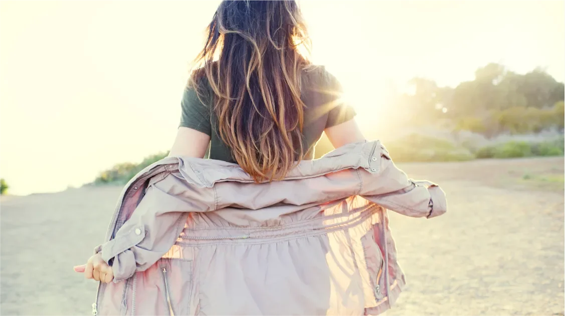 Behind the back shot of a young woman walking towards the sunset