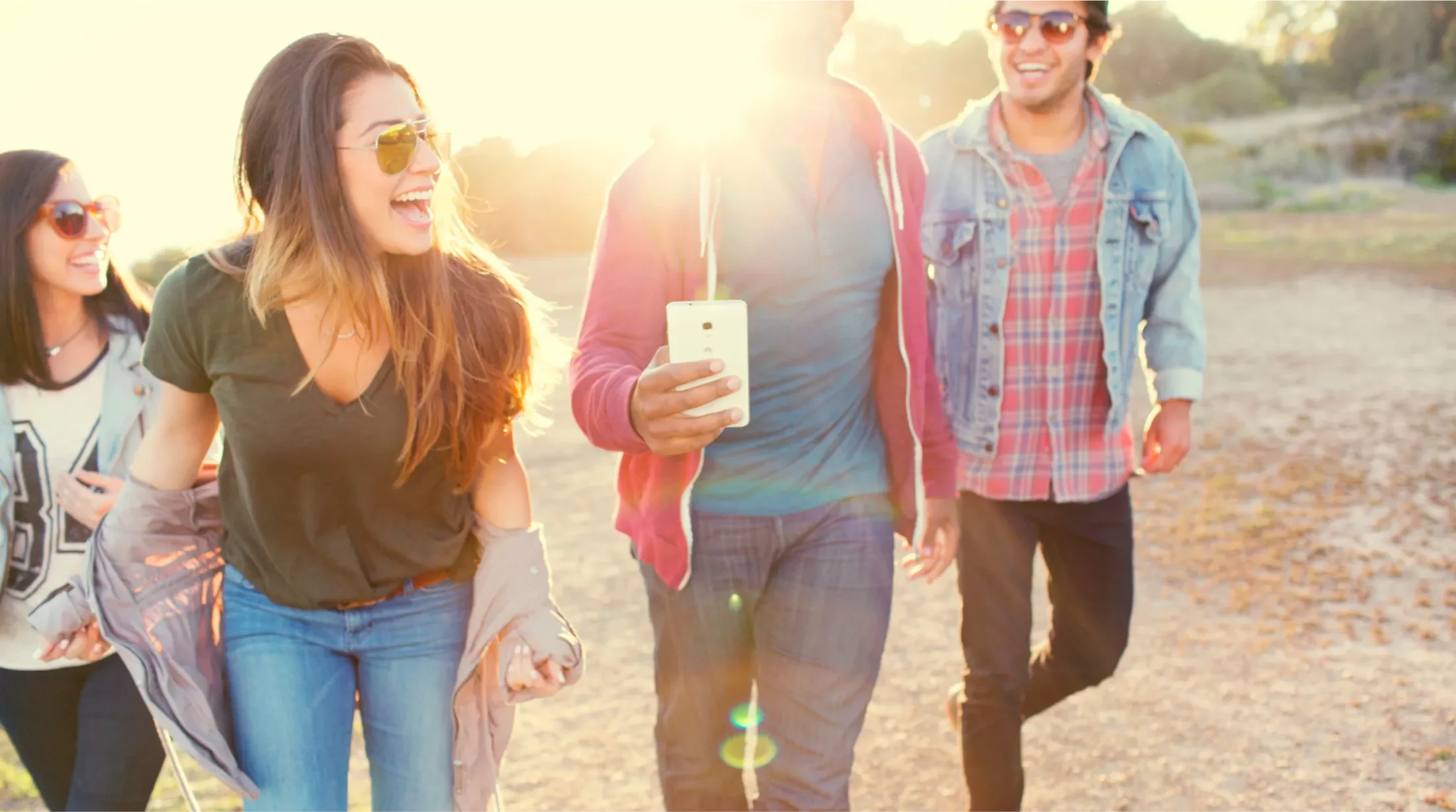 Four young adults obscured by the sun walking through a field, one is holding the Huawei Ascend Mate2