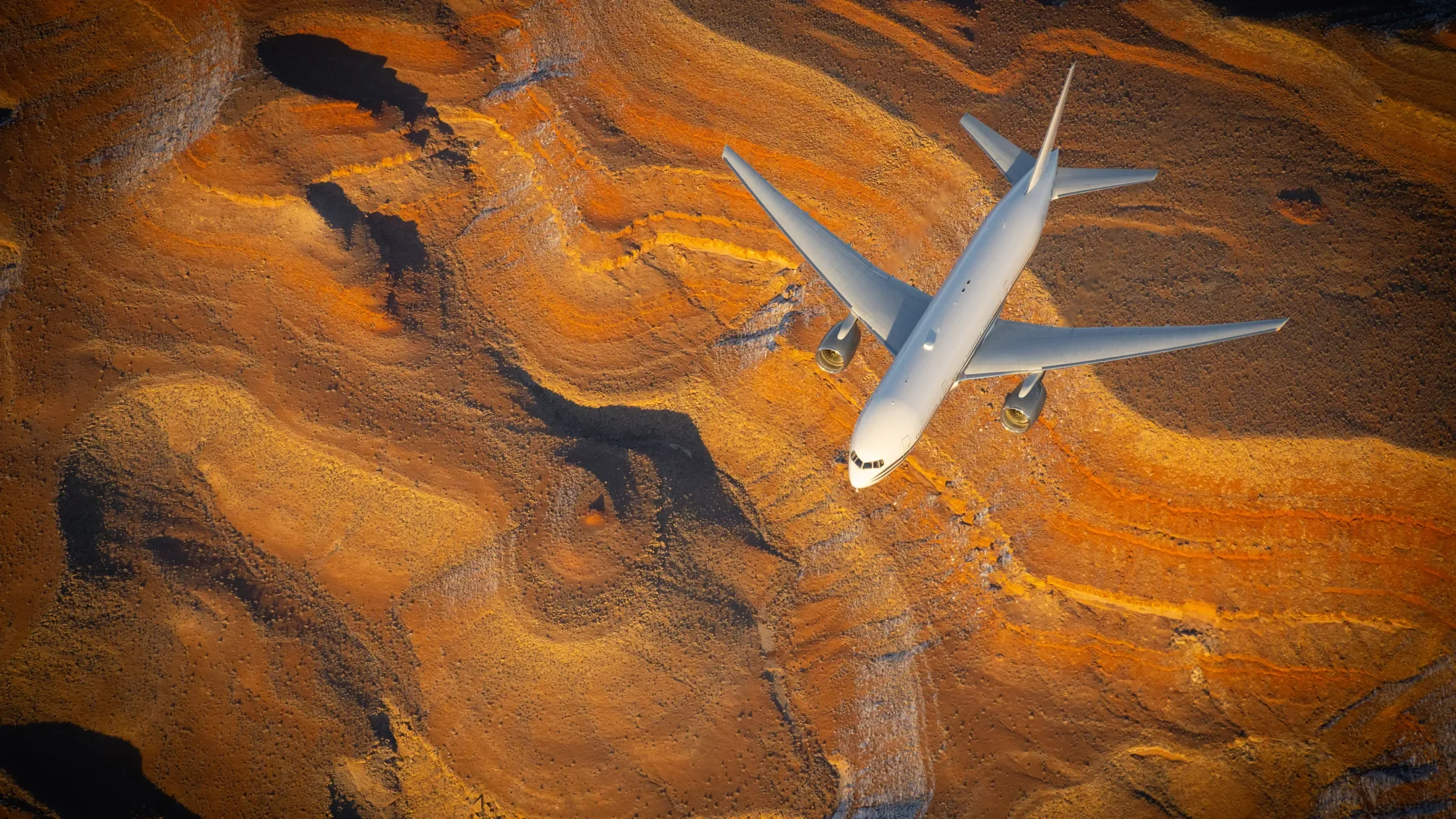 Boeing 777 flies above a bright orange Arizona terrain during sunset.