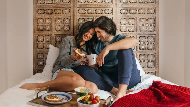 Smiling couple sitting on a bed sharing toast with Laughing Cow cheese spread