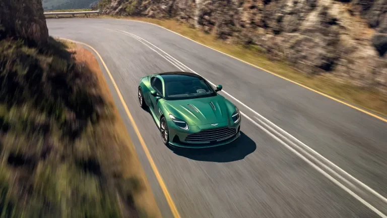 green aston martin speeding down a mountain road