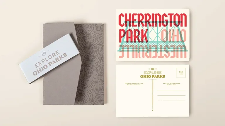 postcard container laid flat with a beli band askew on top, placed next to both the front and back of the Cherrington Park postcard