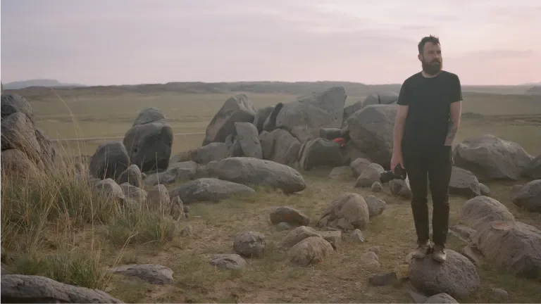 man surrounded by boulders in an open field with a camera by his side