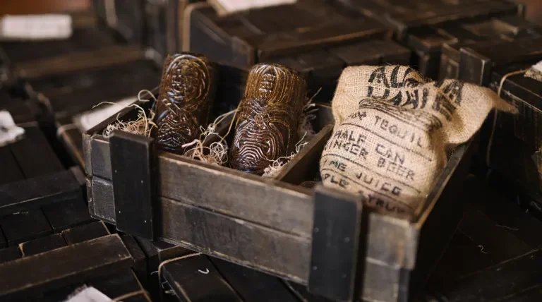 Open wooden box holding two tiki bags and a cloth sack with writing printed on it