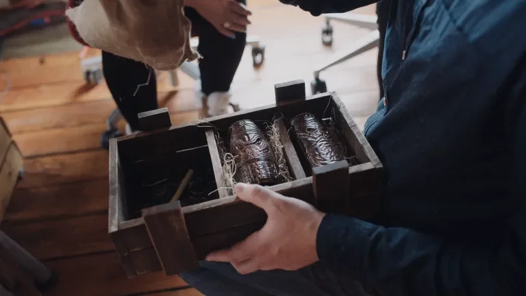 A man holding the wooden packaging holding two tiki mugs while he begins to pack the third and final mug