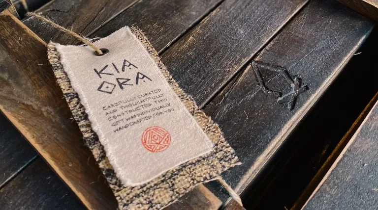 Packaging exterior, close-up on the bonfire brand and the screenprinted cloth tag which reads "Kia ora carefully crafted and thoughtfully constructed this gift was individually handcrafted for you"