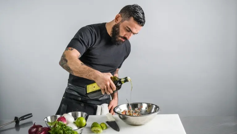 Man pouring oil into a bowl with salad in it
