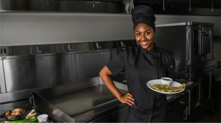 Smiling chef in a kitchen holding a plate of food