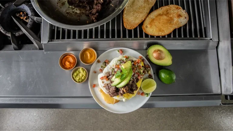 Plate of food near the stovetop with toasted bread, dips and two avocados nearby
