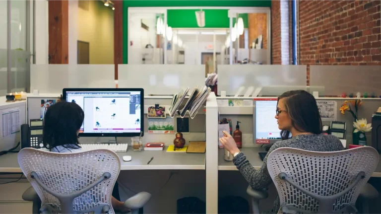 Baesman office shot of two women colleagues talking in their cubicals