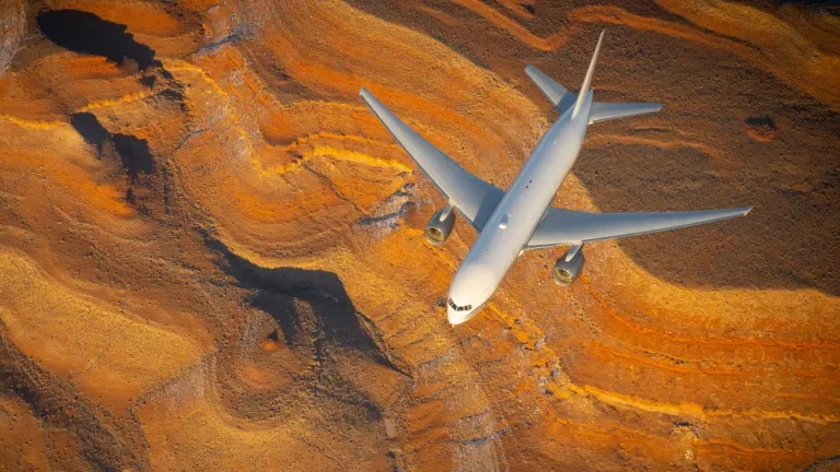 Boeing 777 flies above a bright orange Arizona terrain during sunset.