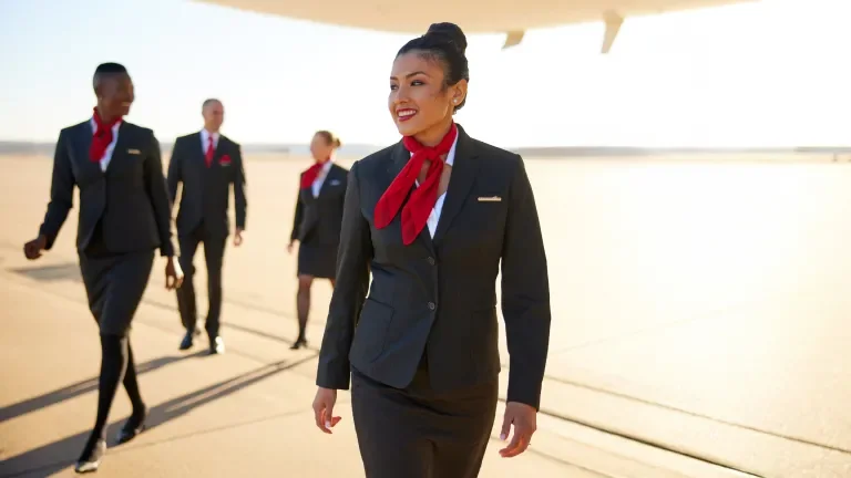 Gridiron Air flight attendants walk on a tarmac under the belly of a Boeing 777 at sunset.