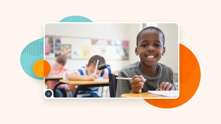 Image of three children in classroom setting, sitting at desks. Child in foreground is using a wheelchair.