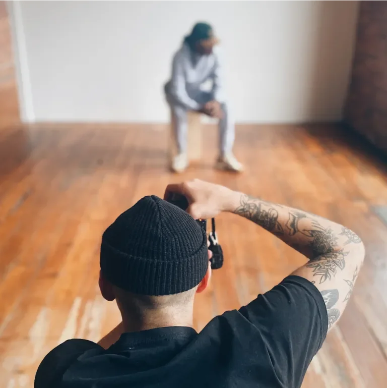 Man taking a photo of someone sitting on a chair in front of a white wall
