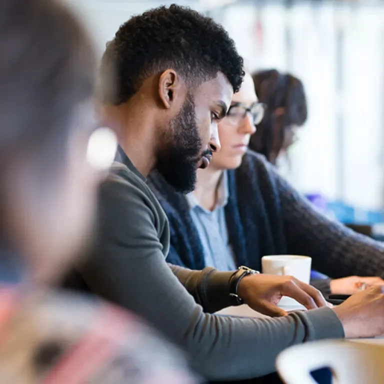 A man in a room of people looking down at a paper on his desk