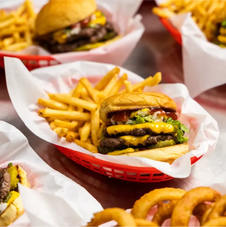 Several cheeseburgers with fries in red baskets