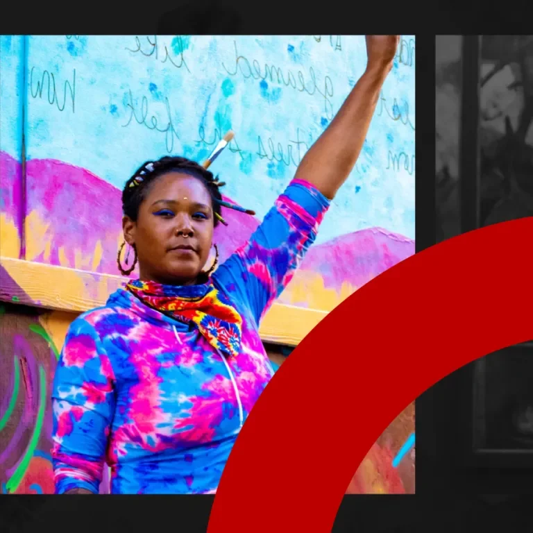 A woman in a pink and blue tie die hoodie against a multi-colored background holding up a fist