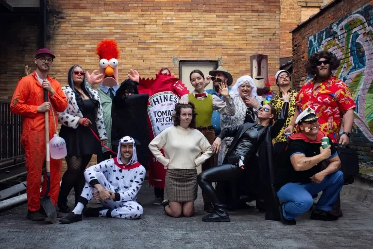 The Bonfire Red team dressed in various costumes posing in a graffitied alley for their 2025 Halloween event