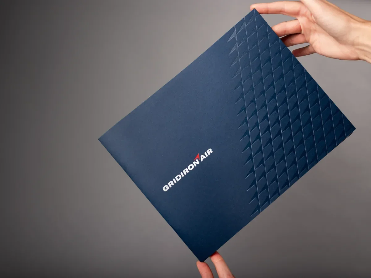 Two hands holding a navy brochure with the Gridiron Air logo on the cover